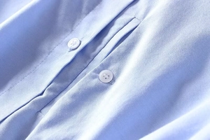 Macro shot of light blue Oxford fabric texture with fine stitching and white buttons