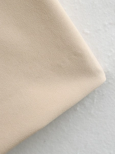 Détail macro du tissu beige de la robe montrant la texture fine et l'élasticité