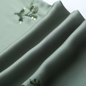 Detailed close-up of sage green satin fabric with intricate sequin leaf embroidery