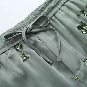 Detail of sage green satin pants with elastic waist, drawstring, and sequin embroidery