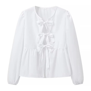Detail of white long-sleeve blouse featuring three front bows and ruffled peplum hem