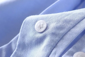 Macro detail of light blue oxford fabric texture and white button on long sleeve shirt