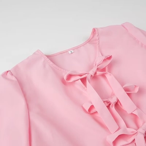 Detail of pink blouse showing round neck and three decorative bows on woven fabric