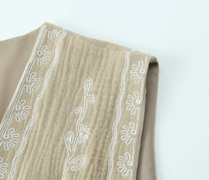 Gros plan détaillé de la broderie florale sur gilet en lin beige avec tissu texturé