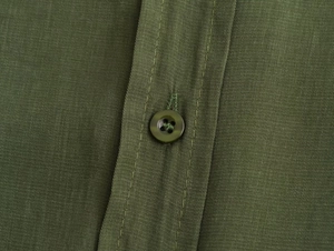 Macro detail of army green linen blend fabric with matching four-hole resin button