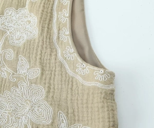 Détail de la broderie florale sur tissu crépon beige avec motifs ondulés rétro