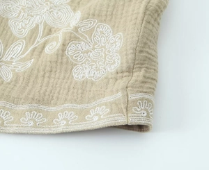 Détail de broderie florale et bordure ondulée sur gilet sans manches beige à texture gaufrée