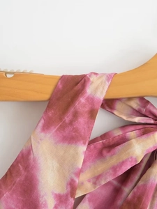 Detail of tie-dye halter dress in pink and beige fabric hanging on a wooden hanger