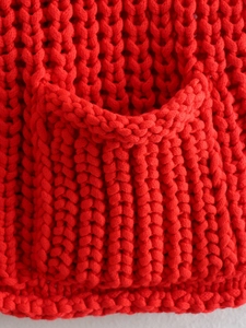 Macro view of bright red chunky knit vest showing the textured stitch and functional pocket