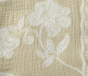 Gros plan sur tissu mousseline kaki avec broderie florale blanche délicate et texture
