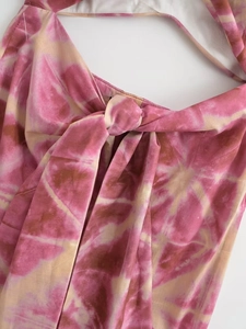 Detail of the halter neck design featuring a pink and beige tie-dye knot on woven fabric