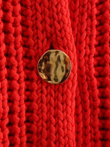 Macro detail of red chunky knit sweater featuring an irregular hammered gold metal button