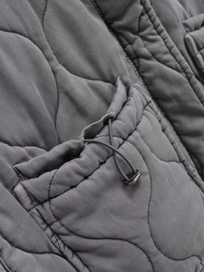 Dettaglio del gilet trapuntato grigio scuro con coulisse regolabile e fermacorda in metallo