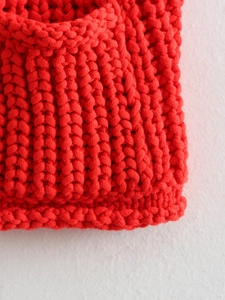 Close-up of red chunky knit vest showing thick vertical ribbed texture and wool fabric