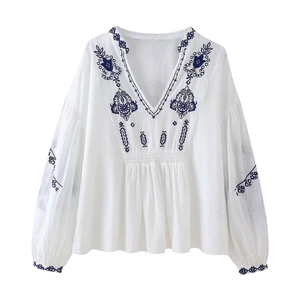 Détails de broderie florale bleue et encolure en V plissée sur un chemisier blanc