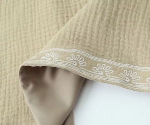 Gros plan du tissu seersucker kaki avec broderie florale blanche et bords ondulés