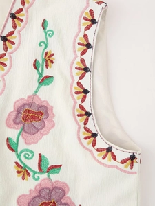 Detailed view of colorful flower embroidery and pink scalloped trim on white vest