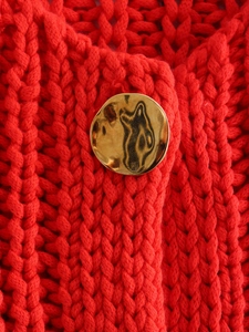 Detail of chunky red knit fabric featuring a textured gold hammered metal button