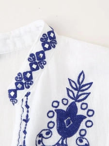 Détail de broderie ethnique bleue et paillettes miroir sur chemise blanche en coton