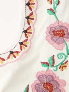 Close-up of vibrant floral embroidery on a white vintage short vest with textured fabric