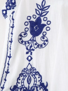 Détail de la broderie florale et des miroirs sur la chemise blanche à manches longues
