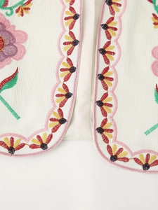 Close-up of floral embroidery on cream vest with pink wavy scalloped edges and detailed textures