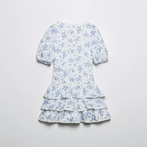 Detailed view of white floral mini dress featuring tiered ruffles and lace trimming