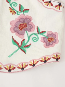 Close-up of intricate floral embroidery and wavy pink stitching on the white cotton fabric