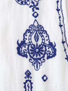 Vue macro de la broderie bleue et des détails miroir sur une chemise en coton blanc