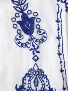 Gros plan de la broderie florale bleue bohème et détails miroir sur tissu en coton blanc