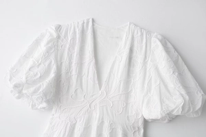Détail de la broderie florale 3D et des manches bouffantes d'une robe blanche à col en V