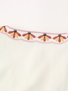 Macro shot of colorful floral embroidery and scalloped pink edging on a white vest collar