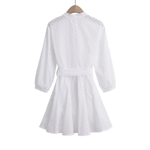 Detail of white long sleeve dress showing intricate eyelet embroidery and matching fabric belt