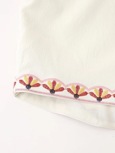 Detailed view of pastoral flower embroidery and pink scalloped edge on beige vest fabric