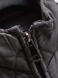 Detail view of the metallic zipper and diamond quilting on a dark grey padded jacket