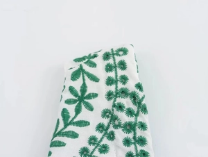 Macro detail of intricate green floral embroidery on white summer dress fabric