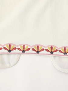 Detail shot of colorful scalloped embroidery on a white cotton vest with floral texture