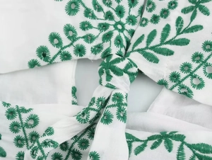 Detail of white cotton dress with green floral embroidery and front tie knot design