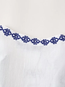 Détail du col en V avec broderie ethnique bleue et petits sequins miroir sur tissu blanc