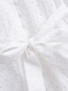 Detailed view of white eyelet embroidery dress with buttons and waist bow tie