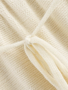 Detailed macro view of the cream knitted fabric texture with decorative drawstring ties