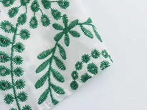 Detailed macro view of green floral embroidery and eyelet cutouts on white fabric