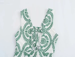 Close-up of deep V-neckline with green leaf embroidery on white sleeveless fabric