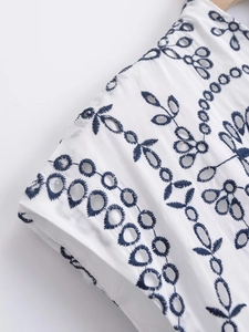 Detail view of navy floral embroidery and eyelet hollow cut on white cotton fabric dress