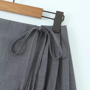 Detail of dark grey pleated skirt showing side zipper and decorative ribbon bow knot