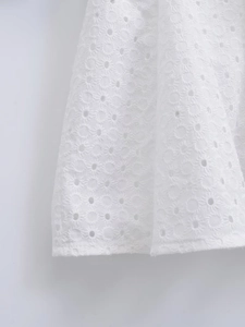 Detailed close-up of white broderie anglaise fabric with intricate embroidery and eyelet design