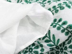 Detail view of white fabric with green leaf embroidery and delicate hollow out lace design