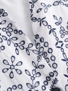 Detailed close-up of white cotton fabric with navy floral embroidery and eyelet cutouts