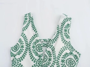 Detail of white dress with green leaf embroidery and V-neckline buckle design