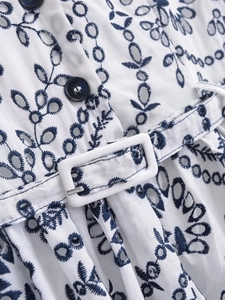 Detail of V-neck summer dress featuring blue embroidery, eyelet lace, and a matching belt buckle